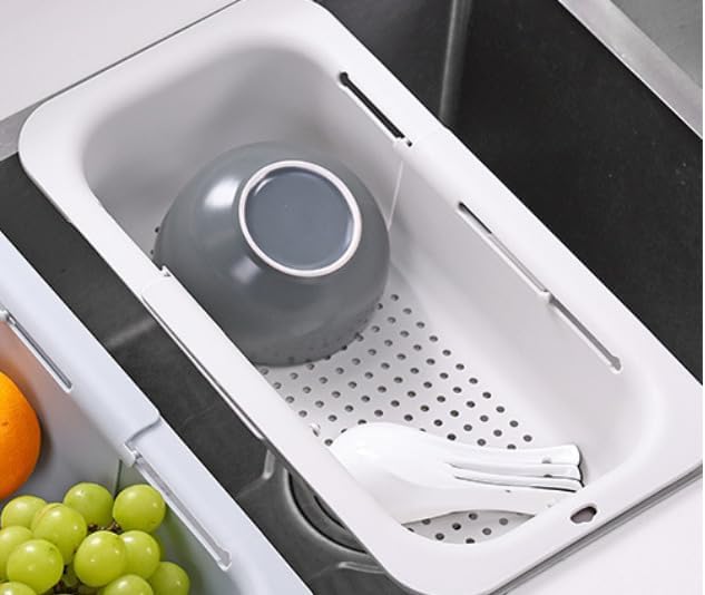 White expandable colander basket sitting across a kitchen sink with vegetables in it